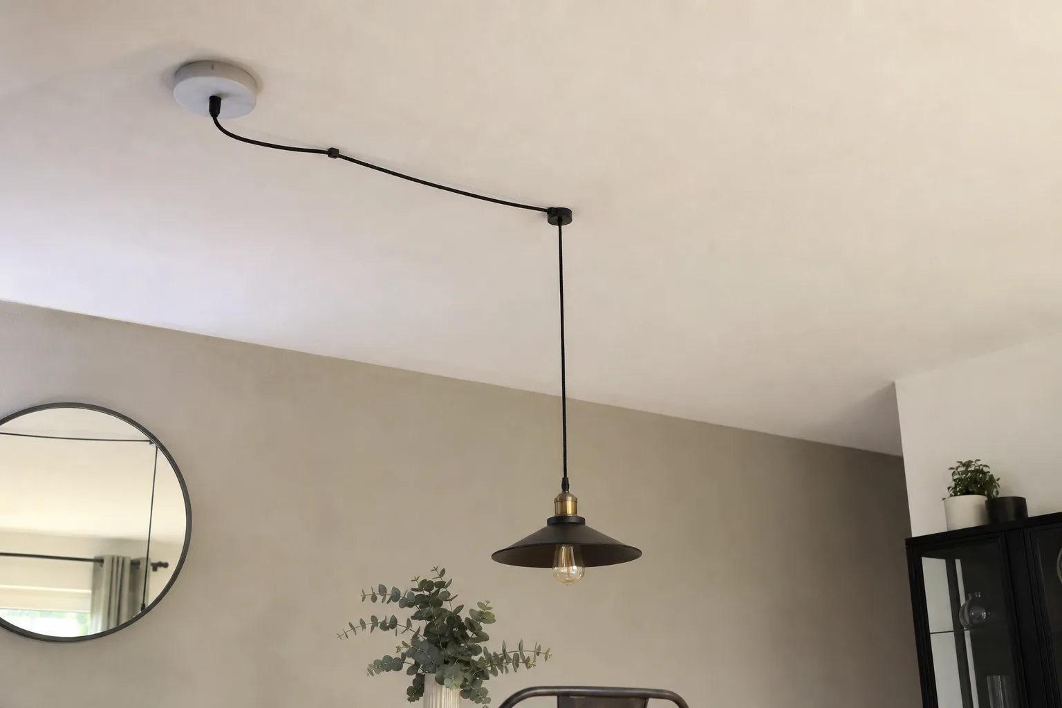 Câble apparent reliant une rosace près du mur à une suspension située au-dessus d'une table.