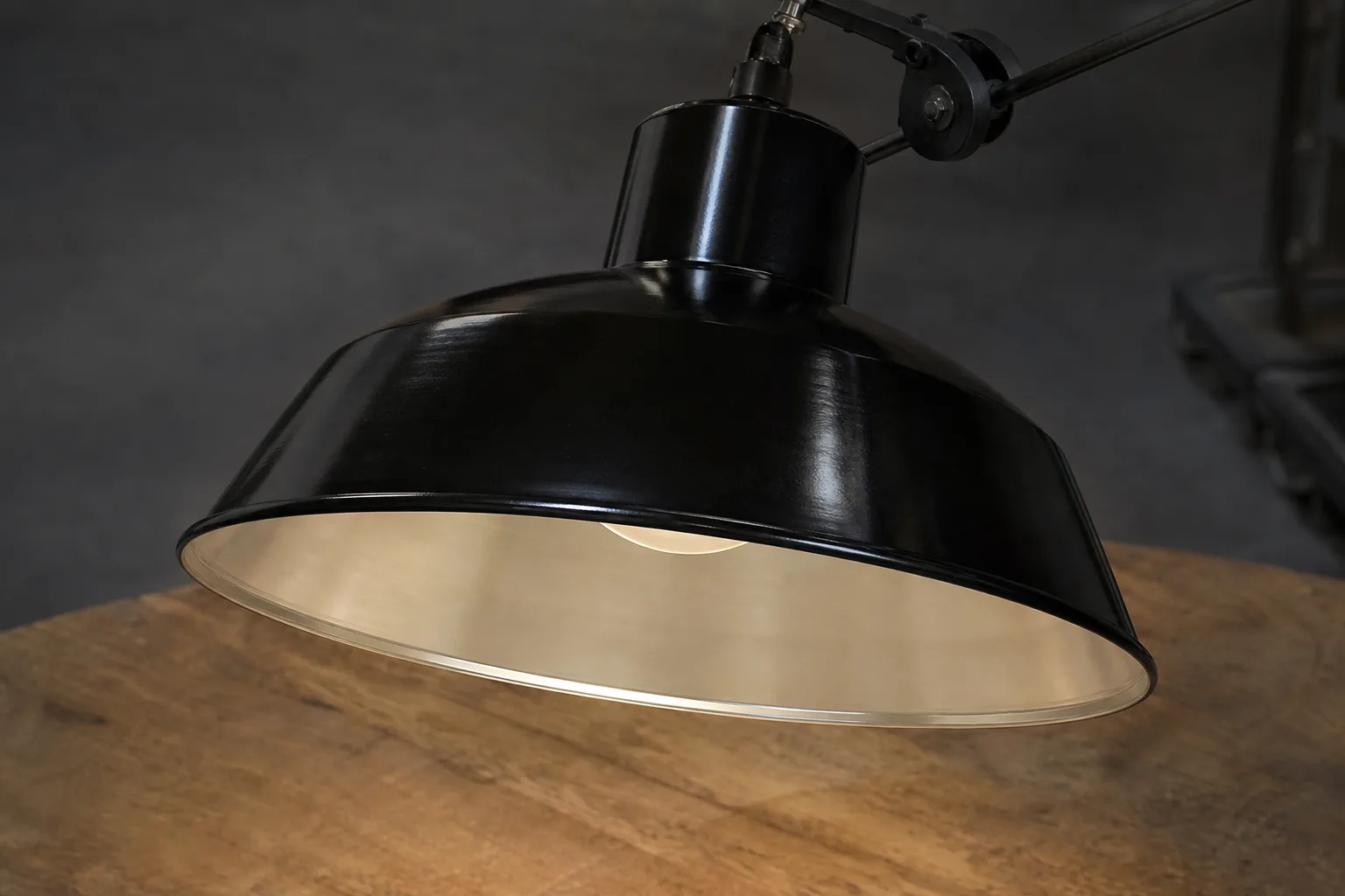Abat-jour industriel noir en forme de dôme, avec son intérieur clair visible au-dessus d’une table.