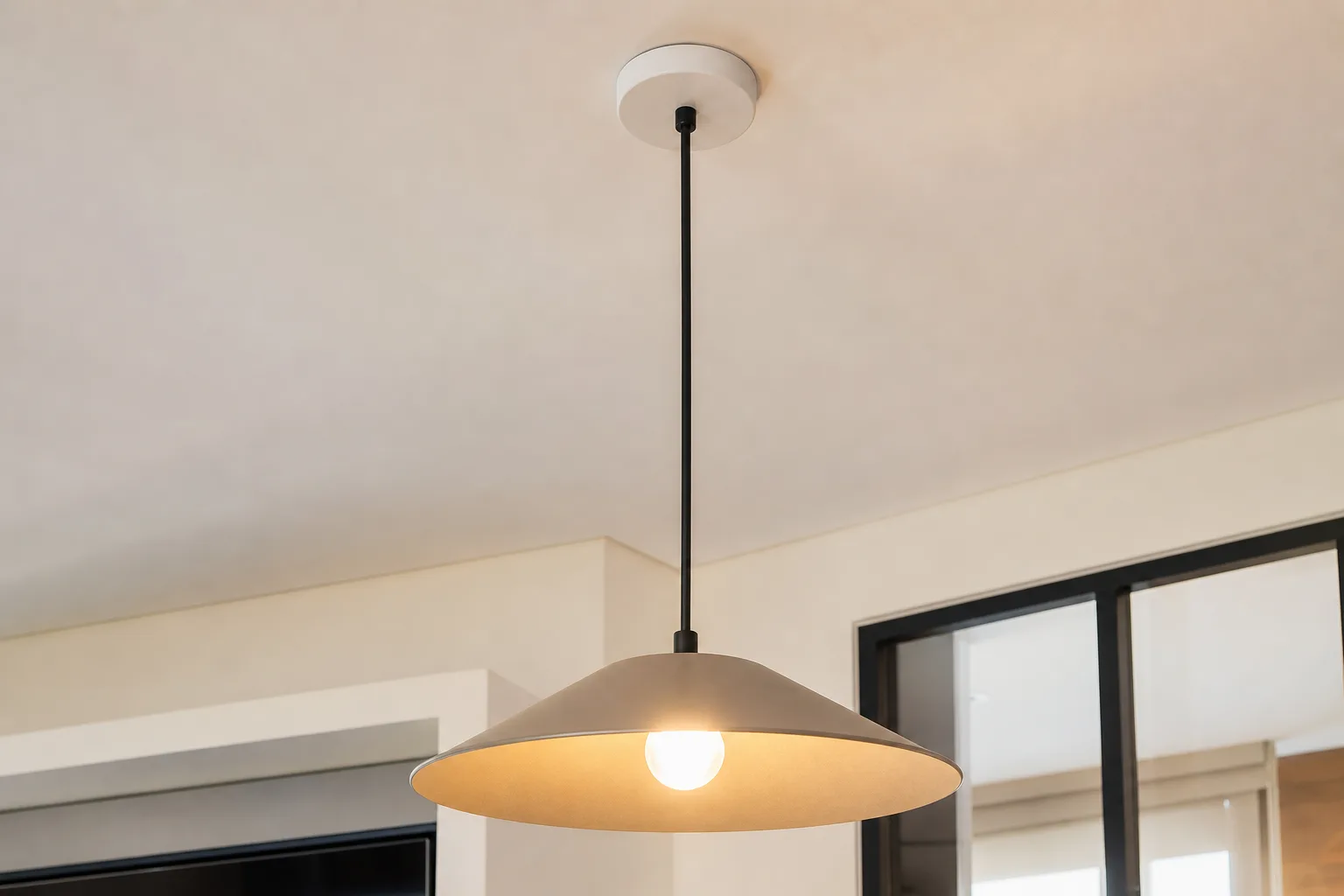 Suspension à abat-jour clair fixée par une rosace sur un plafond blanc au-dessus d’une table.